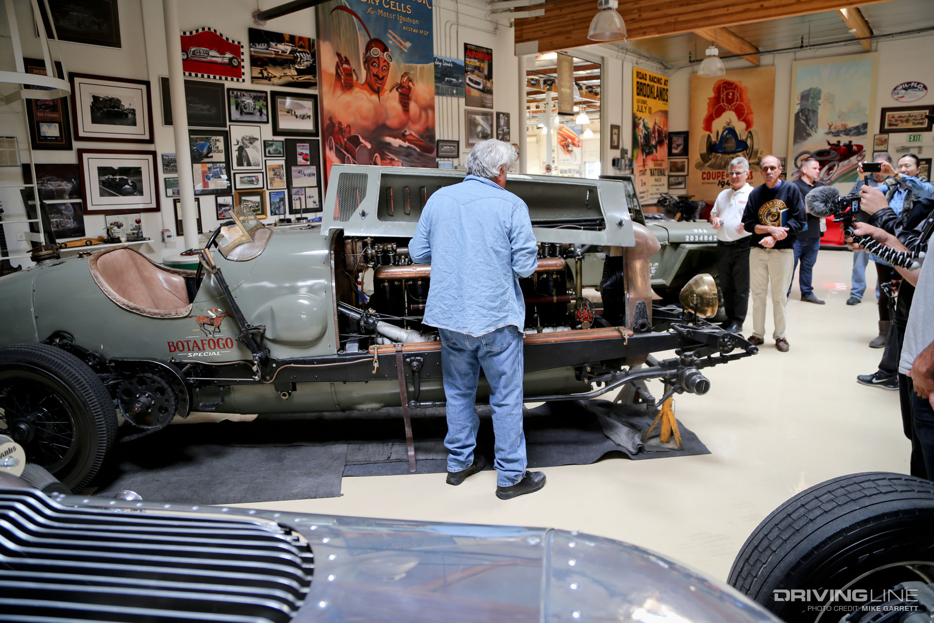 Jay Leno working on the engine of an old, grey car in his garage