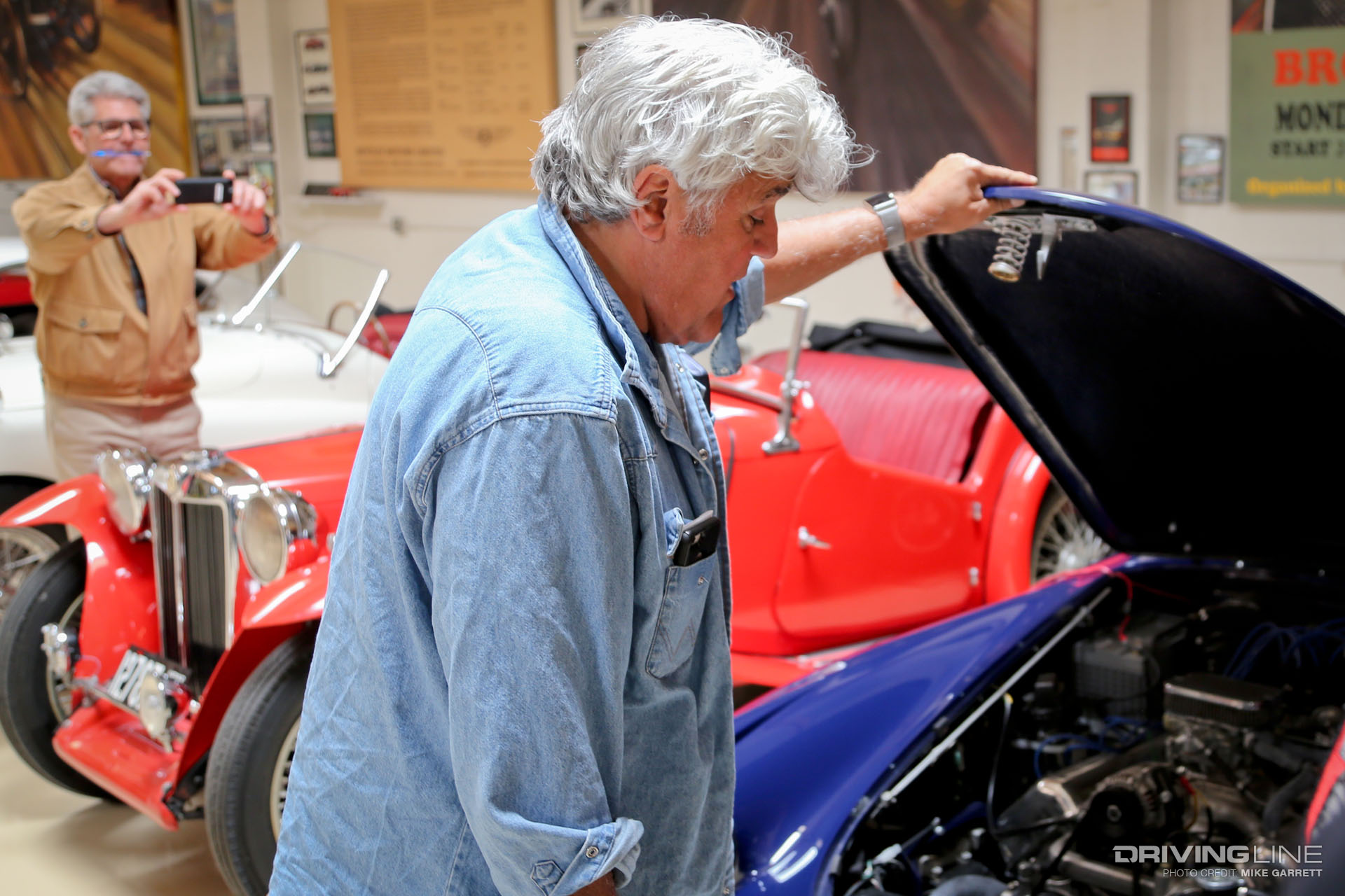 Jay Leno looking under the hood of a blue car